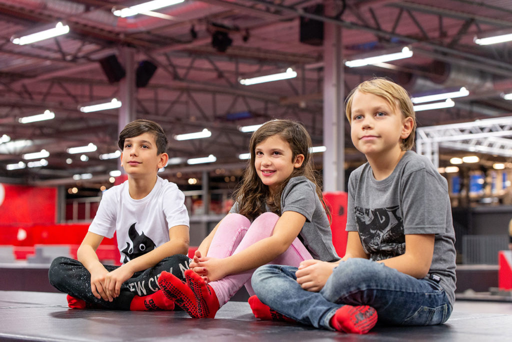 barnaktivitet skövde där Tre barn sitter på golvet i trampolinparken JumpYard. De ser glada ut.